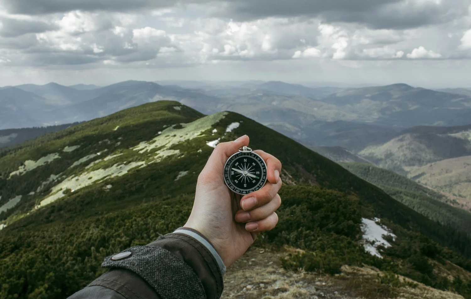 A person holding a compass in front of a mountainous landscape